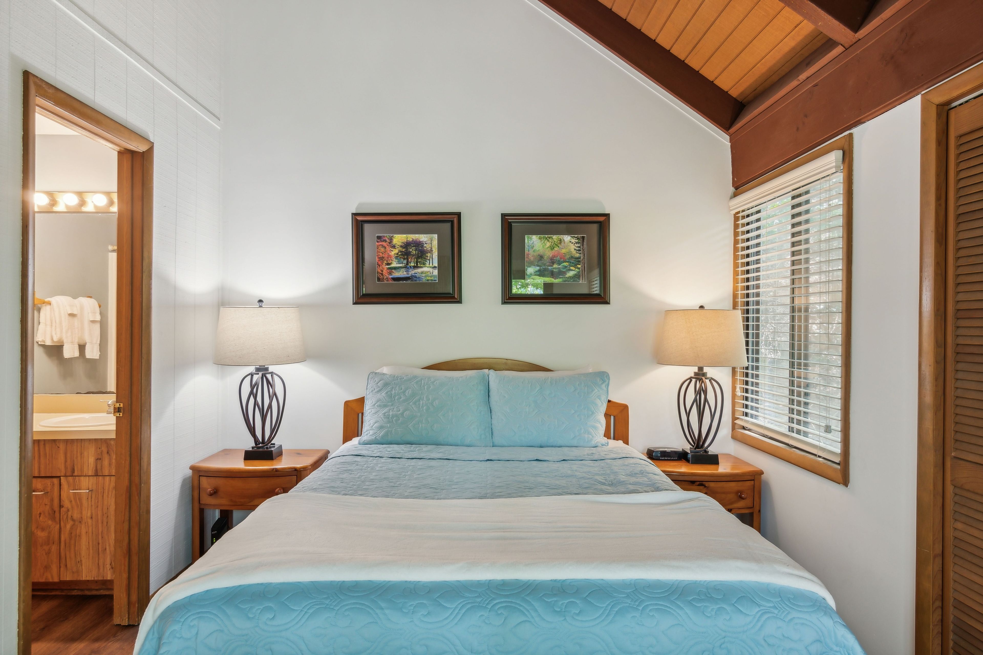 A bedroom with a bed, two bedside tables, a nightstand, a mirror, and two framed pictures on the wall.