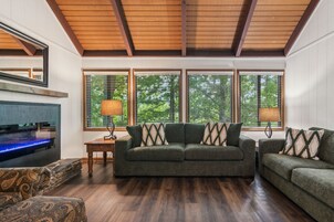 Una sala de estar con techo de madera, un televisor grande, un sofá verde y un reposapiés estampado.