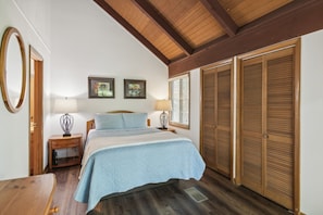 A bedroom with a bed, two bedside lamps, a wooden nightstand, a wooden table, a mirror, and a wardrobe.