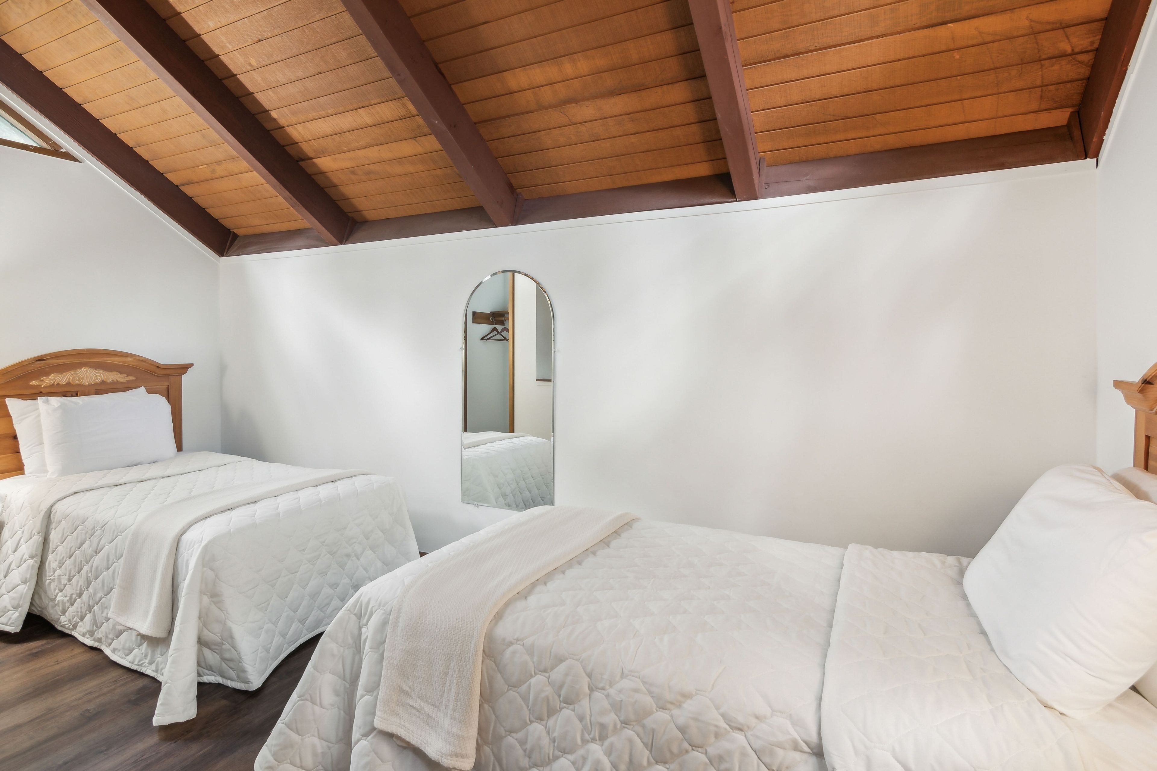 Un dormitorio con dos camas, vigas de madera en el techo y un espejo.