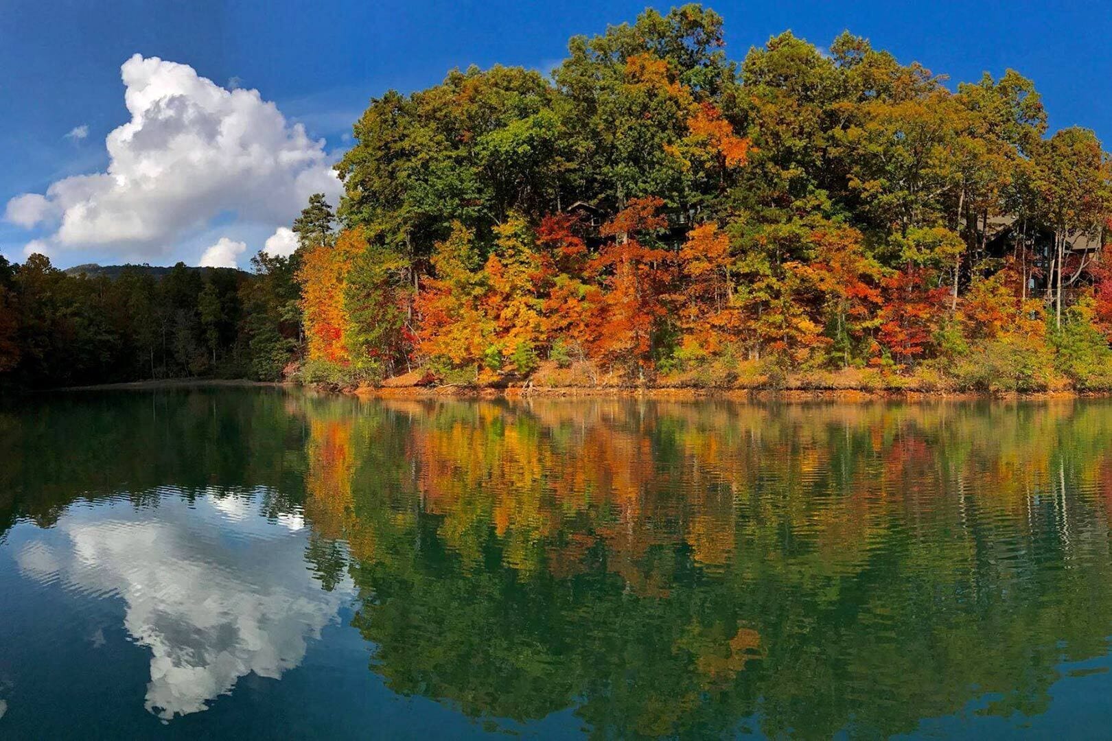 A calm lake with autumn foliage reflecting on the water, surrounded by trees.