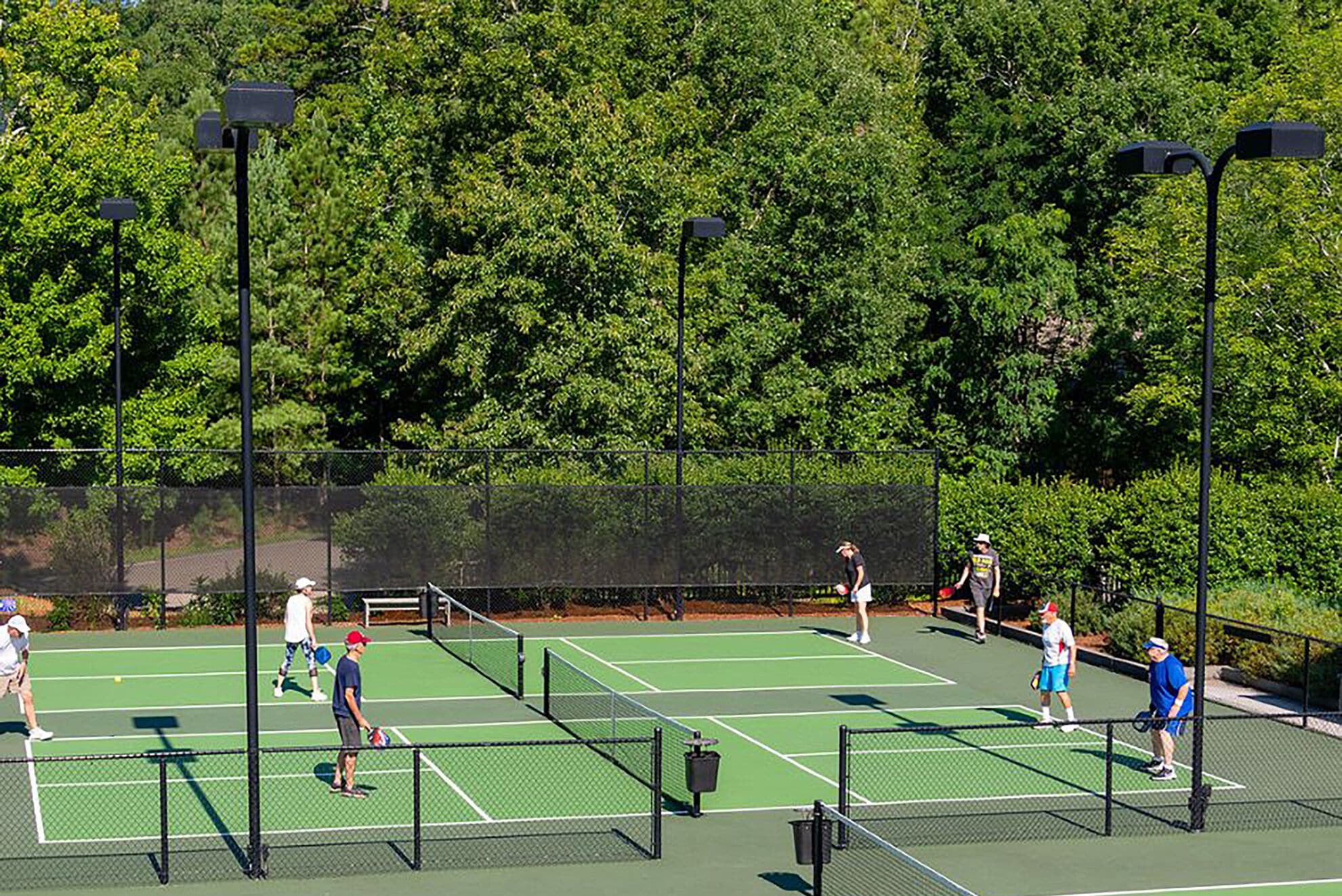 A tennis court with multiple players, surrounded by a fence and trees.
