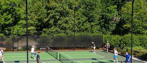 A tennis court with multiple players, surrounded by a fence and trees.
