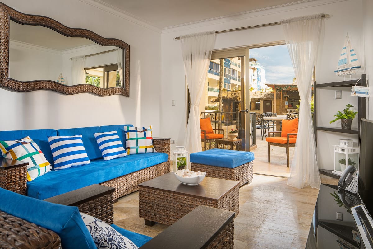 A living room with a blue sofa, wicker furniture, and a view to an outdoor dining area.
