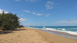 A sandy beach with footprints leading to the water, a clear sky, and a distant mountain. - Playa Laguna Beach Condos (Cabarete)