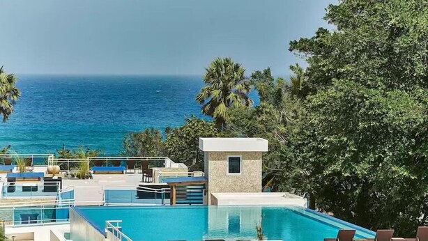 A pool area with a view of the ocean, lounge chairs, and a small building. - Playa Laguna Beach Condos (Cabarete)