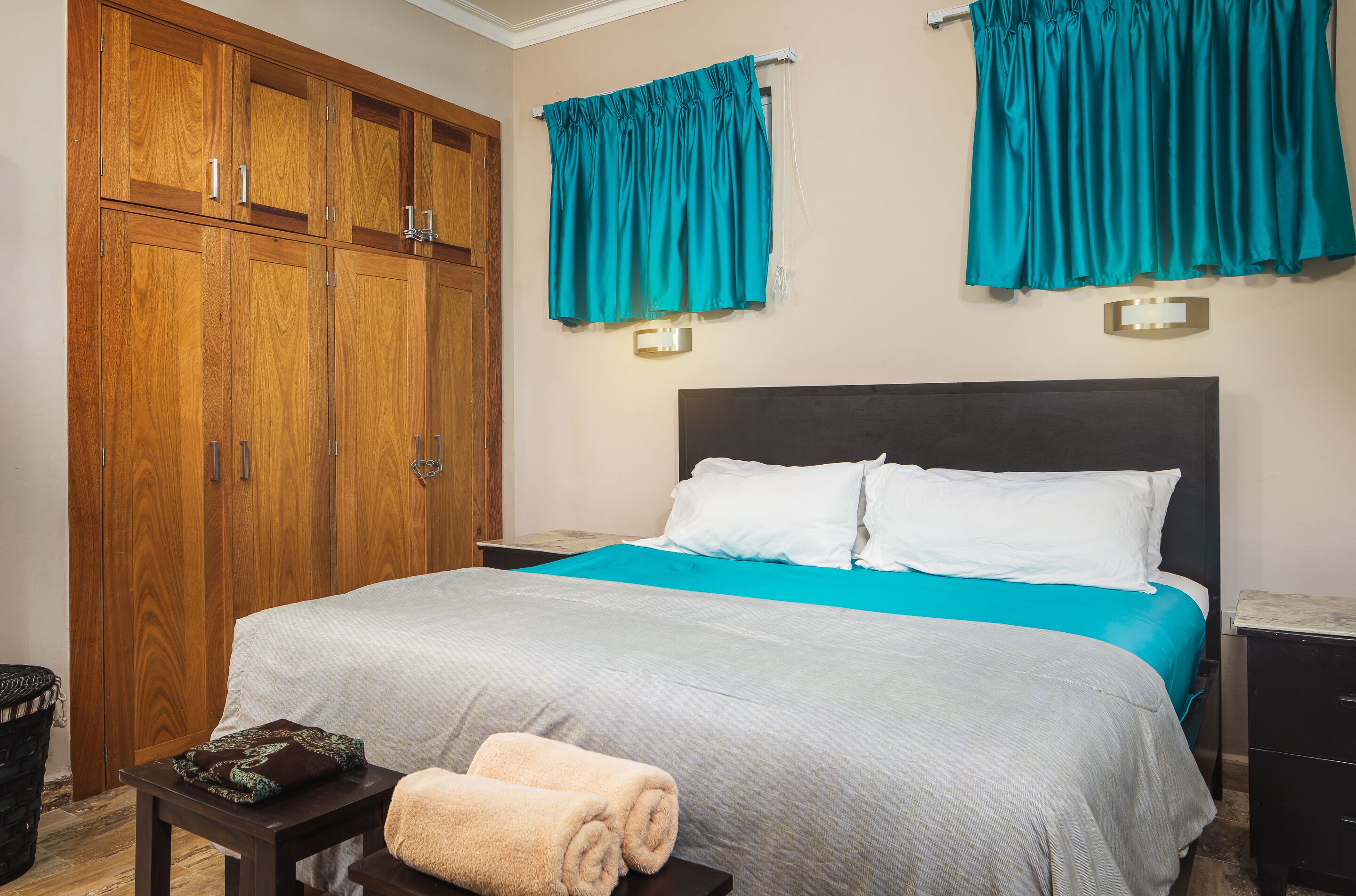 A bedroom with a bed, a wooden wardrobe, and teal curtains.