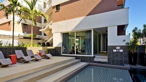 A modern building with a swimming pool, outdoor seating, and a staircase leading to the entrance. - Apartamento de Frente pro Mar - Campeche (Florianópolis)