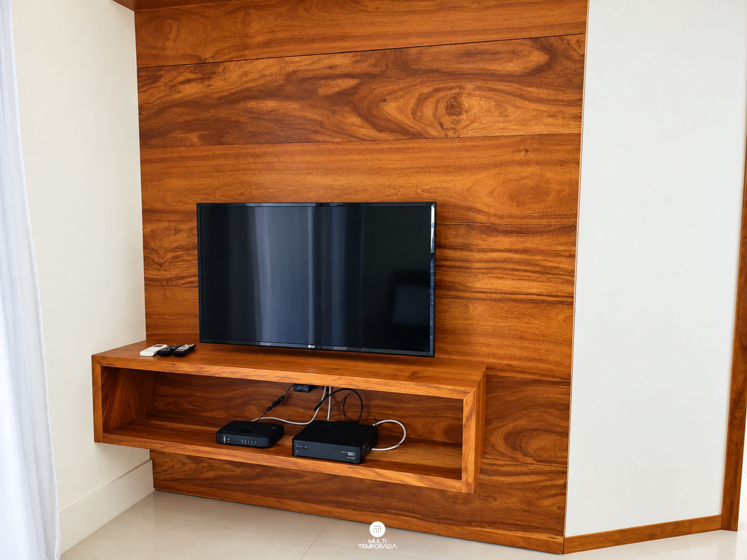 Un televisor de pantalla plana montado en una pared de madera, con un estante inferior que sostiene dos dispositivos electrónicos.