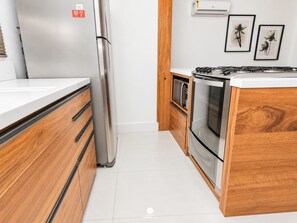 Cozinha moderna com geladeira de aço inoxidável, armários de madeira, forno embutido e bancada branca.