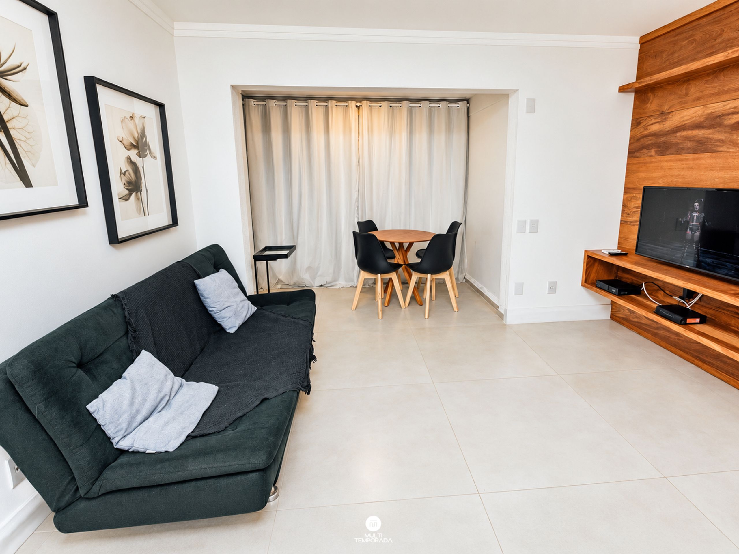 Una sala moderna con un sofá verde oscuro, un mueble bajo para televisión de madera y una zona de comedor con una mesa y sillas.