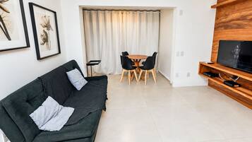 Una sala moderna con un sofá verde oscuro, un mueble bajo para televisión de madera y una zona de comedor con una mesa y sillas.