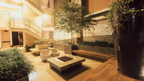 A modern indoor courtyard with a wooden staircase, seating areas, and a large planter. - Apartamento de Frente pro Mar - Campeche (Florianópolis)