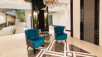 Un vestíbulo moderno con dos sillones turquesa, un candelabro y un diseño geométrico en el suelo.