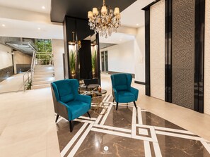 Een moderne lobby met twee teal fauteuils, een kroonluchter en een geometrisch vloerontwerp.
