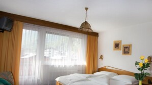 A hotel room with a bed, a chair, a table, a vase with flowers, and a television. - Alpha Hotel (Saas Grund)