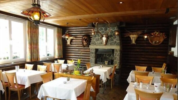 A restaurant with wooden interiors, stone walls, and a fireplace. Tables are set with white tablecloths and chairs. - Alpha Hotel (Saas Grund)