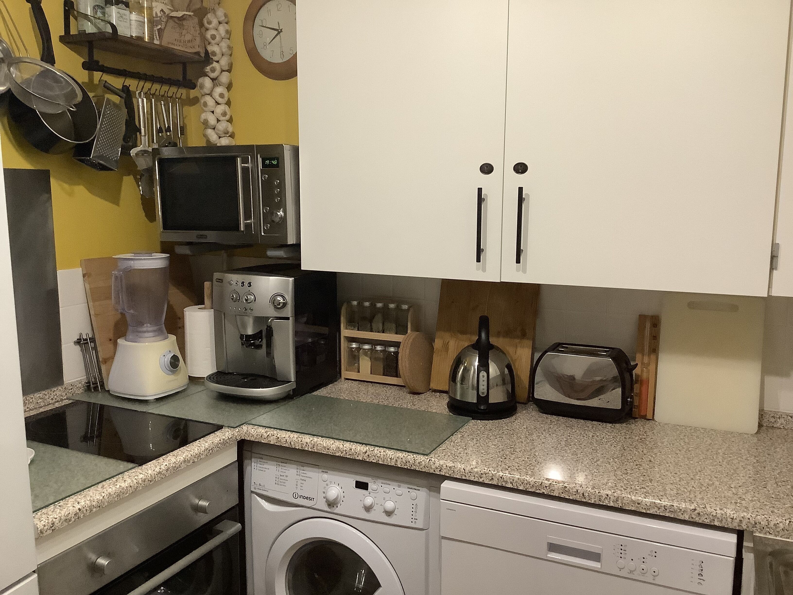 Een kleine keuken met een magnetron, koffiezetapparaat, waterkoker, broodrooster en een wasmachine.