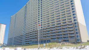 Un grand hôtel avec de nombreux balcons, un mât de drapeau et une plage en premier plan.