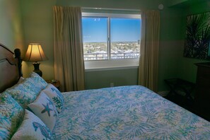 Une chambre à coucher avec un lit, une fenêtre avec des rideaux, une lampe et une vue sur un quartier résidentiel.