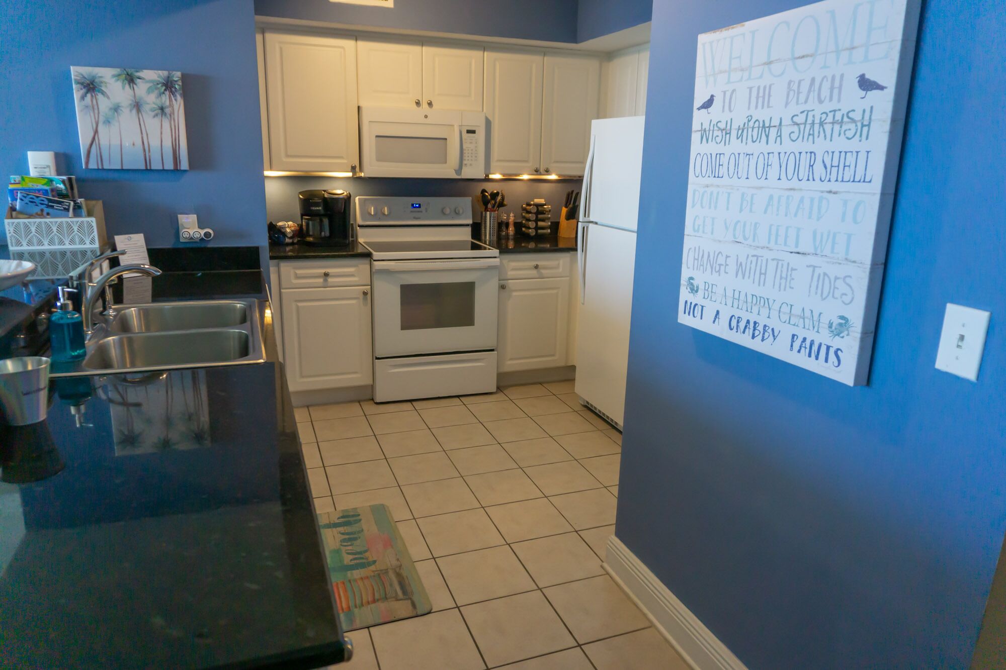 A kitchen with white cabinets, a microwave, an oven, and a refrigerator. There is a sign on the wall with a message about embracing change.