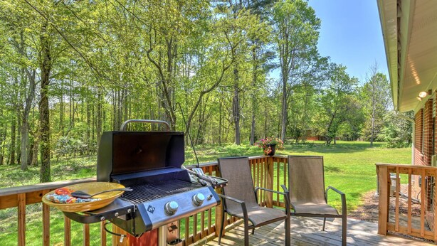 Eine Außenterrasse mit Grill, Stühlen und Blick auf einen Wald.