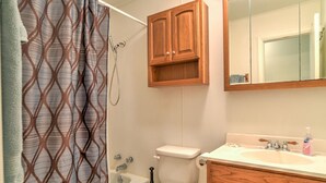 Ein Badezimmer mit Duschvorhang, Toilette, Badewanne, Holzschränken und einem Waschbecken mit Spiegel darüber.