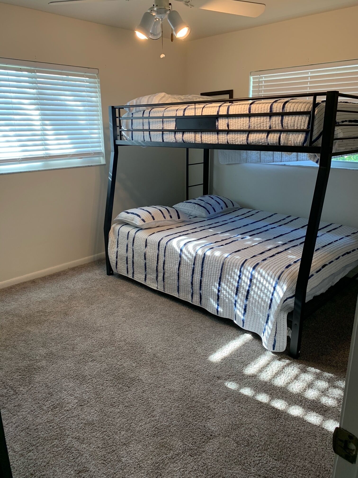 A bunk bed room with a ceiling fan, carpeted floor, and blinds on the windows.