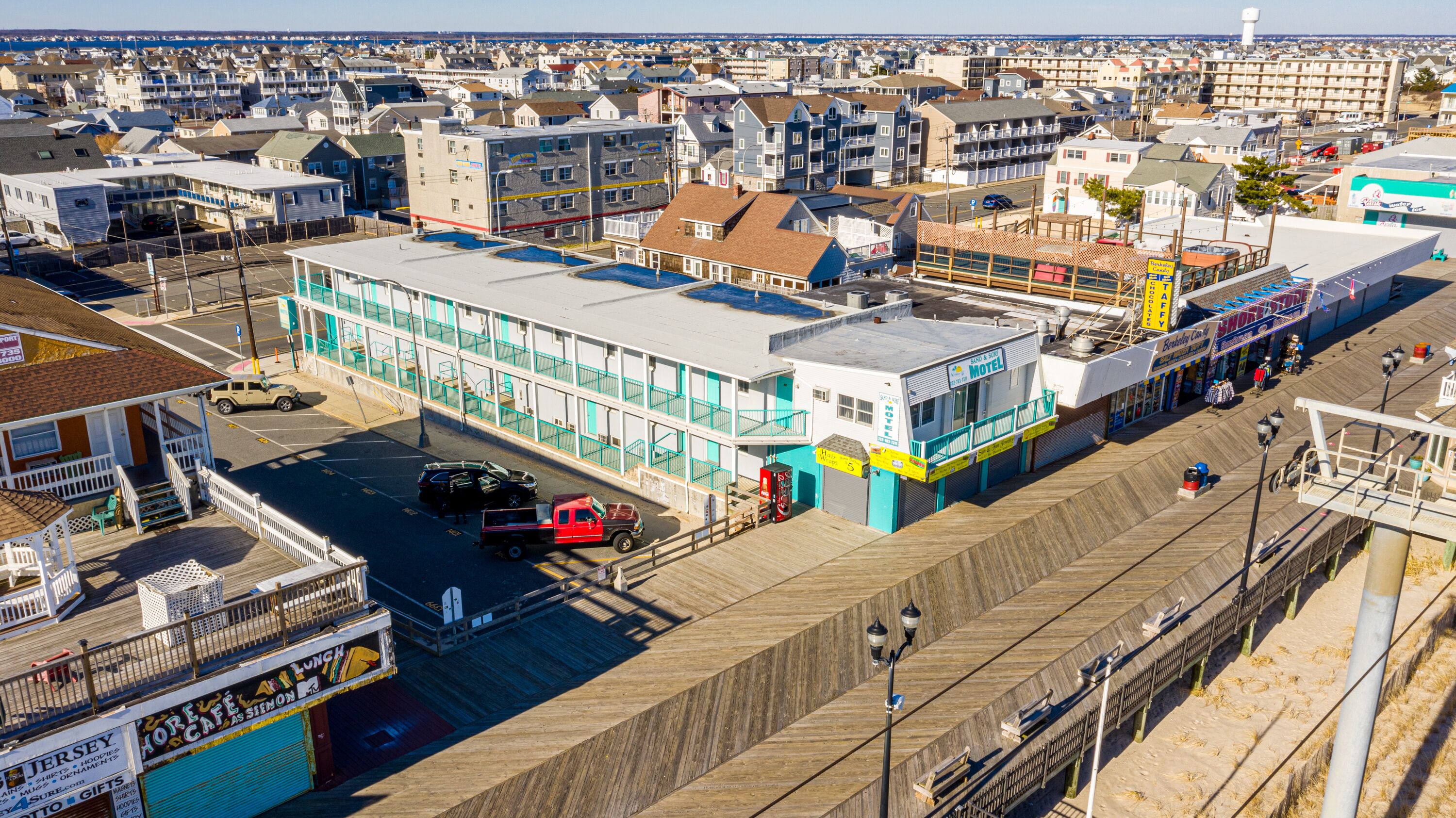 A motel with a large parking lot, a beach boardwalk, and a view of the ocean.