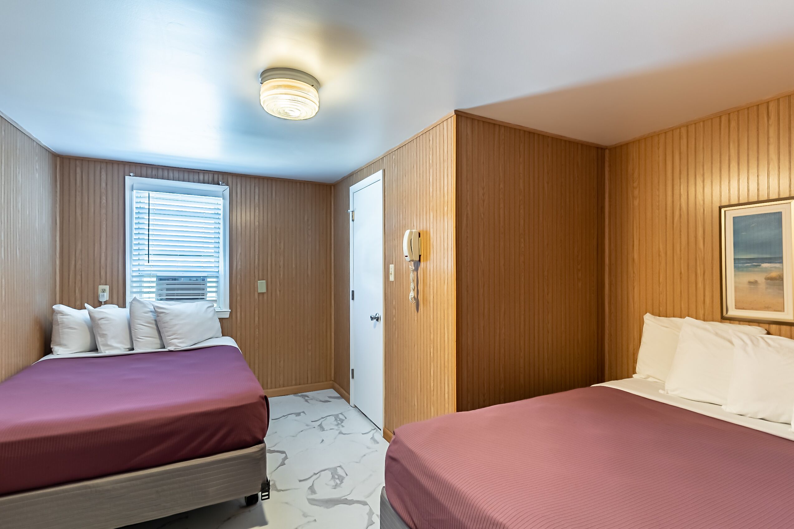 Une chambre d’hôtel avec deux lits, des lambris en bois, une porte et une fenêtre avec des stores.