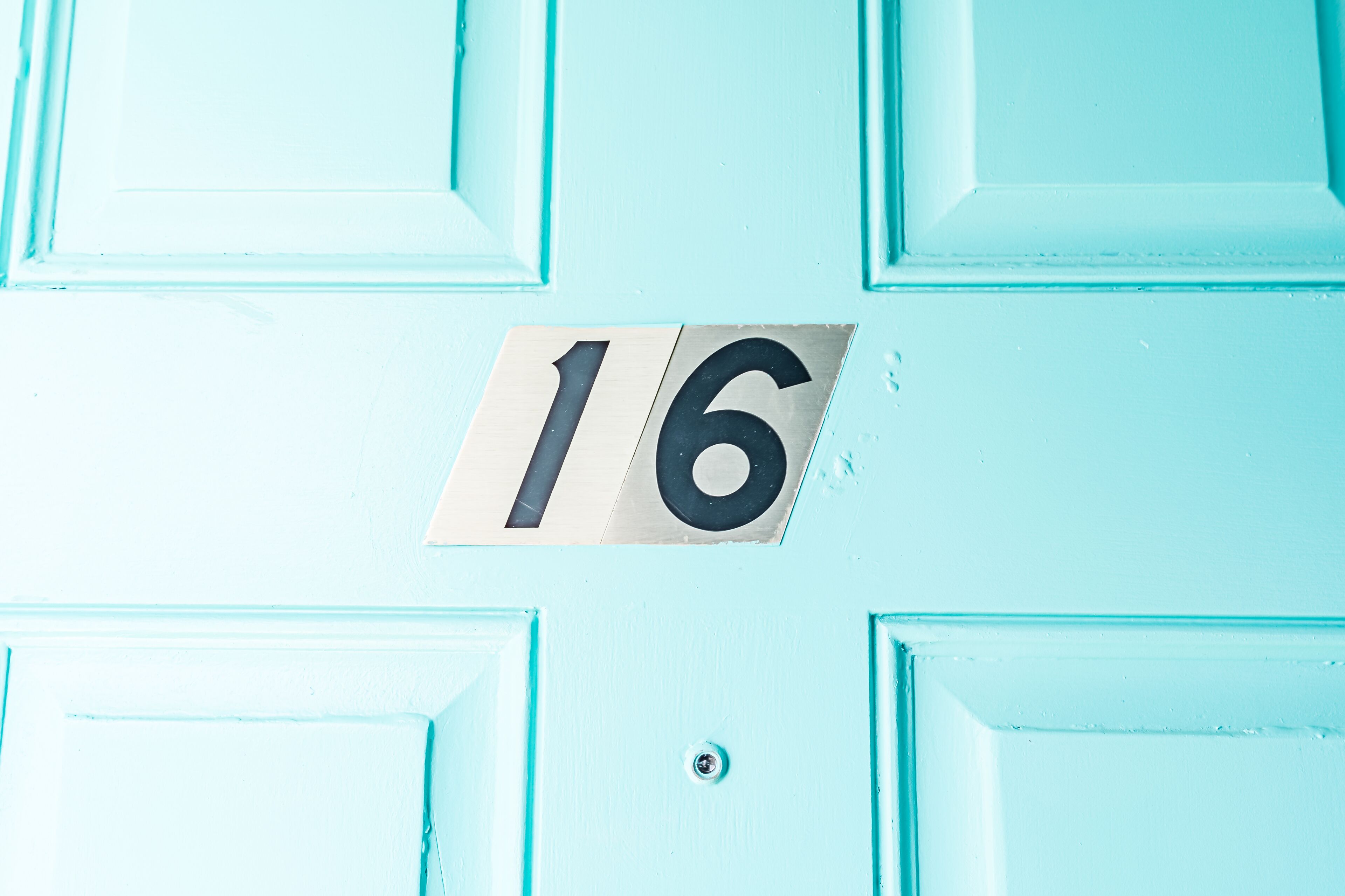 A turquoise door with a number plate displaying the number 16.