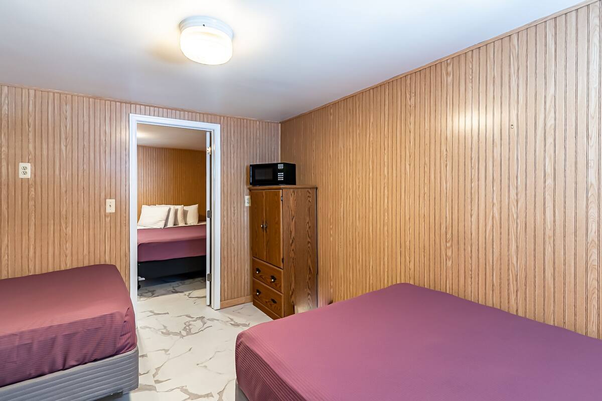 A room with two beds, wooden paneling, a wardrobe, and a microwave.