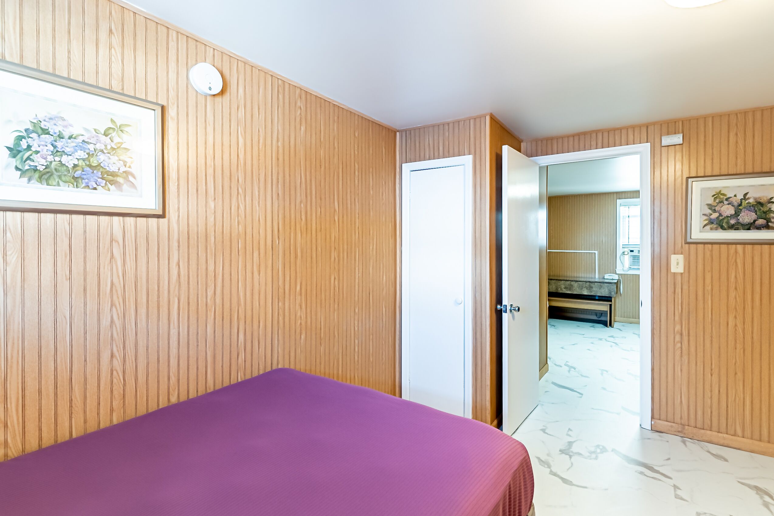 A room with wooden paneling, a purple bed, and a door leading to a bathroom.