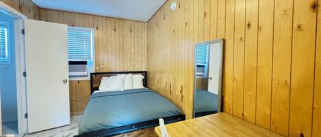 A bedroom with a wooden paneled wall, a bed with a blue mattress, a wooden table, and a mirror.