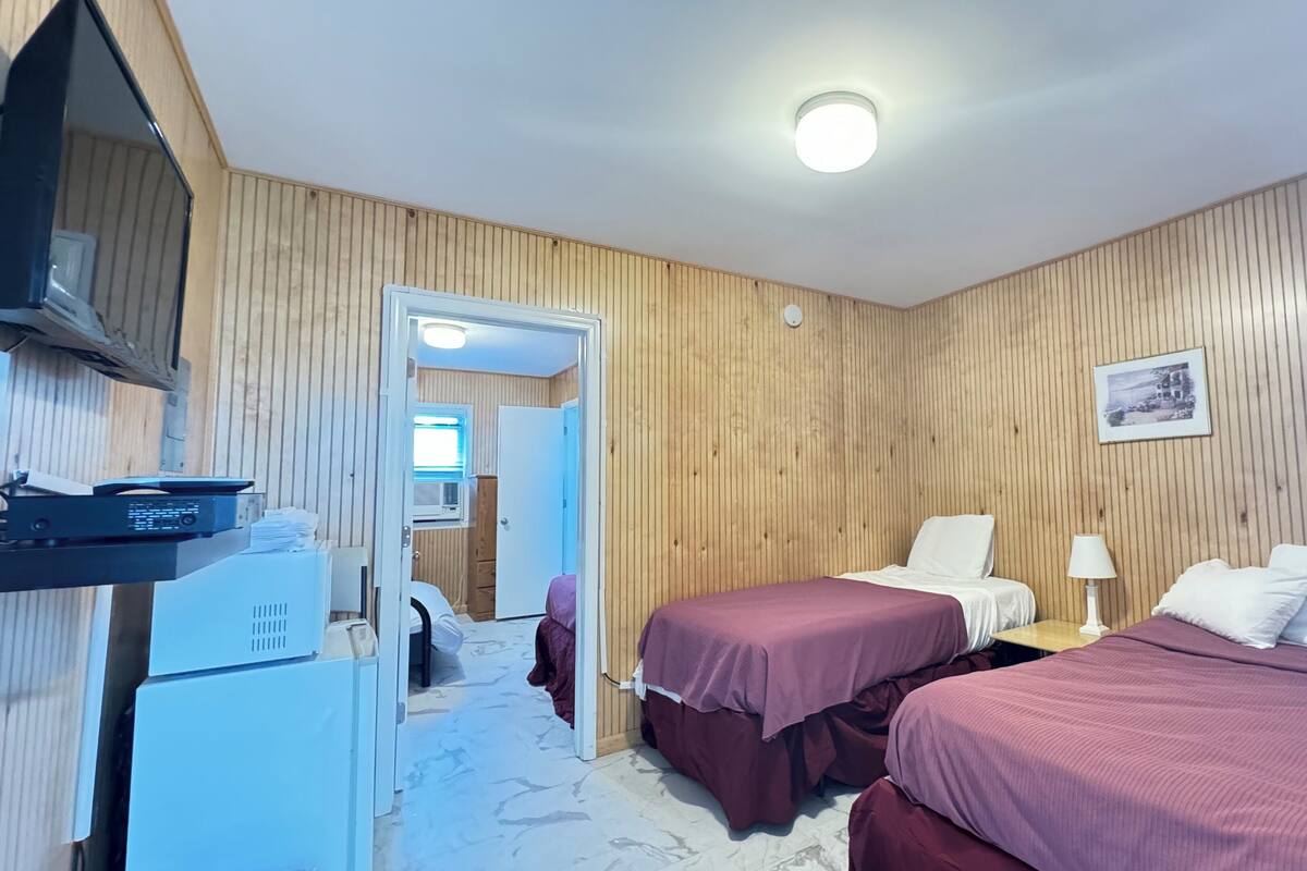 A room with two beds, a desk, a chair, a lamp, and a refrigerator.