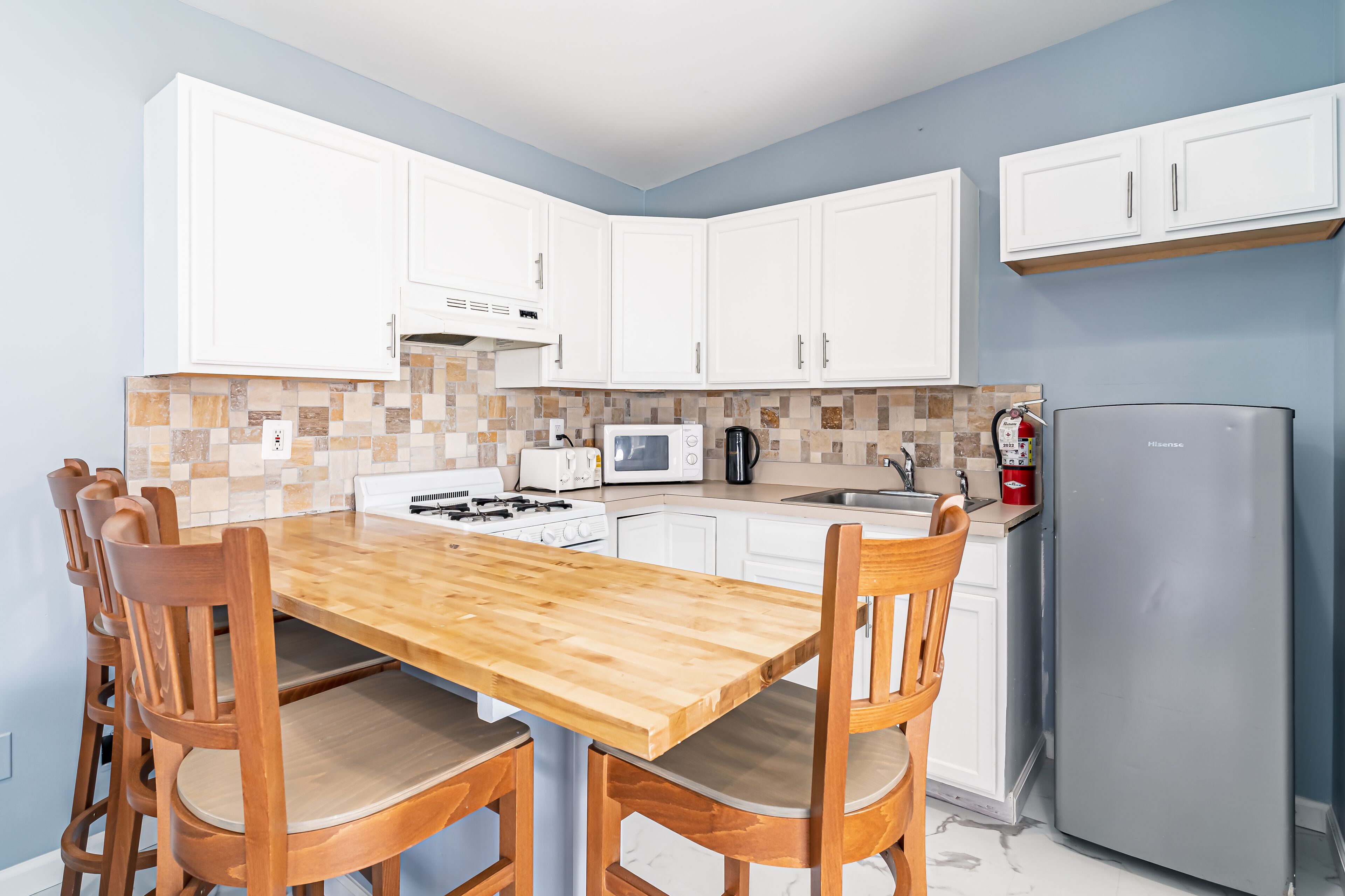 A modern kitchen with white cabinets, a wooden dining table, and a stainless steel refrigerator.