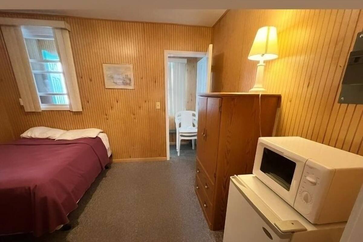 A small, cozy room with a bed, a desk with a lamp, and a microwave.