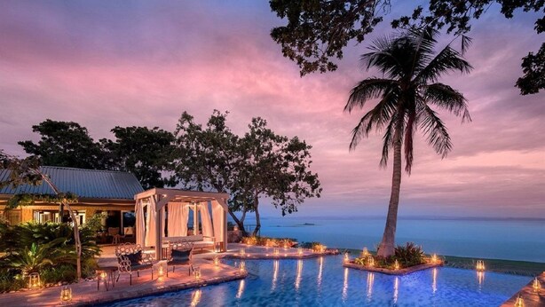A luxurious pool area with a gazebo, palm trees, and a view of the ocean at dusk. - Bumi Hills Safari Lodge (Bumi Hills)