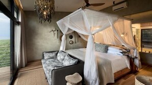 A bedroom with a canopy bed, a chandelier, a ceiling fan, and a view of the outdoors. - Bumi Hills Safari Lodge (Bumi Hills)