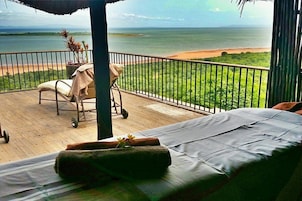 Un balcón con una cama, una silla y un carrito, con vistas a la playa y al océano.