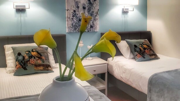 A hotel room with two beds, each with a unique bird-themed pillow. There is a vase with yellow flowers on a nightstand between the beds. - The Inn at Newton Highlands, boutique apartment-hotel (Newton)