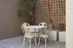 Un ensemble de table et de chaises blanches, placé à l’extérieur, est adossé à un mur orné d’un treillage en bois.