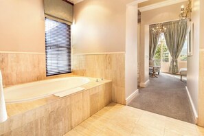 Une salle de bain avec une grande baignoire, une fenêtre avec des stores et une vue sur l’espace repas.
