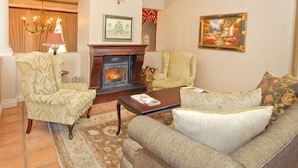 A living room with a fireplace, two armchairs, a sofa, a coffee table, and a chandelier. - L Ermitage Franschhoek Chateau Villas (Franschhoek)
