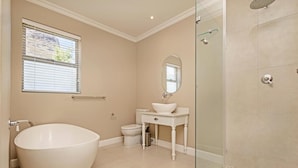 A bathroom with a large freestanding bathtub, a toilet, a sink with a mirror, and a glass-enclosed shower area. - L Ermitage Franschhoek Chateau Villas (Franschhoek)