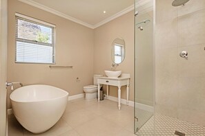 A bathroom with a large freestanding bathtub, a toilet, a sink with a mirror, and a glass-enclosed shower area. - L Ermitage Franschhoek Chateau Villas (Franschhoek)