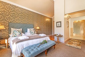 Hotelkamer met een groot bed, een bankje, een klein tafeltje en een badkamer zichtbaar door een geopende deur.