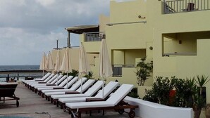 A row of sun loungers with umbrellas, a pool, and a building with balconies overlooking the sea. - Blue Sky Apartments (Hersonissos)
