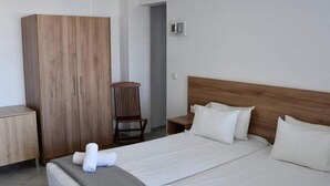 A hotel room with a large wooden wardrobe, a wooden headboard, a single bed with white linens, and a chair. - Blue Sky Apartments (Hersonissos)