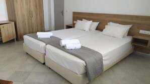 A double bed with two pillows and a blanket, a wooden wardrobe, a bedside table, and a door in a hotel room. - Blue Sky Apartments (Hersonissos)